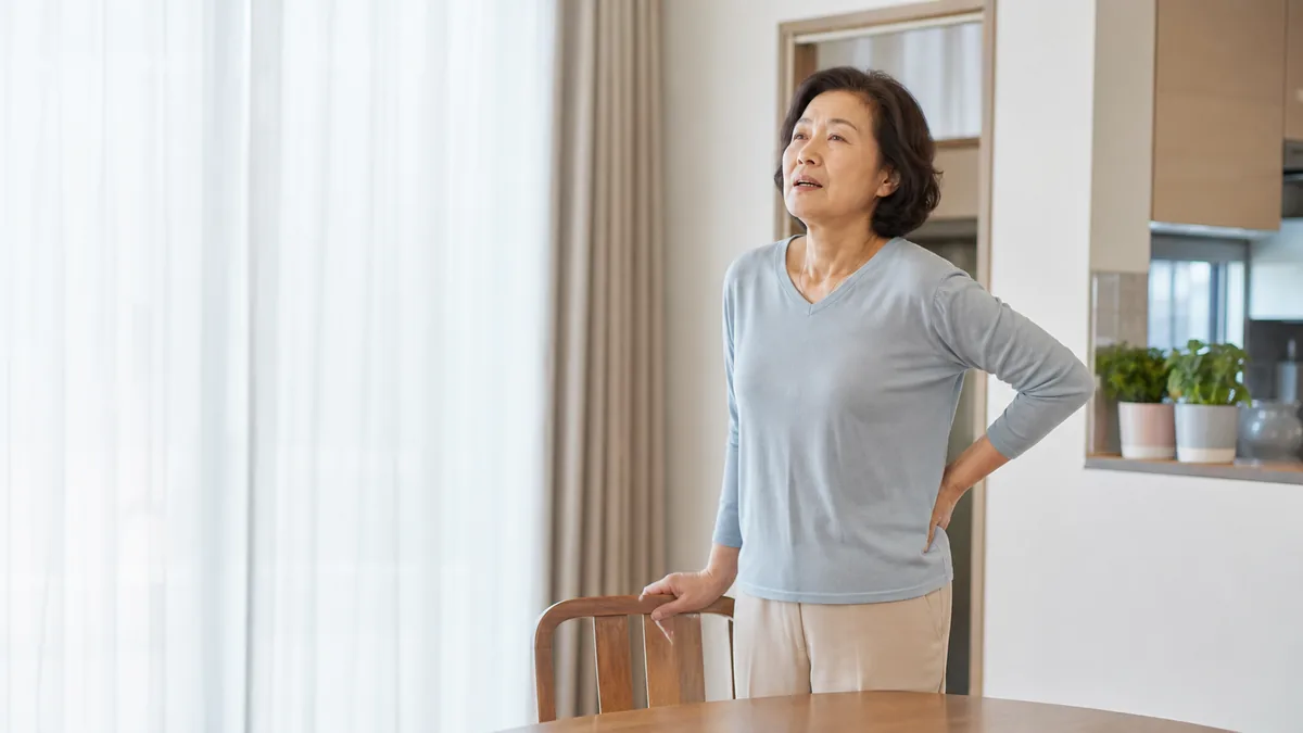 집 창가에서 잠시 멈춰 숨을 고르며 몸 상태를 살피는 중년 한국인