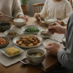 식탁에 앉아 밥과 반찬을 함께 먹는 초등학생 아이와 부모의 저녁 식사 장면