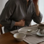 식사를 마친 식탁 앞에서 한 손으로 명치를 누르고 다른 손으로 관자놀이를 짚고 있는 사람