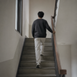 아파트 계단참에서 손잡이를 잡고 위층으로 올라가는 사람의 뒷모습