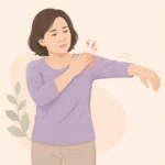 중년 여성이 한쪽 어깨를 손으로 감싸며 팔을 옆으로 들어 올리려다 멈춘 모습