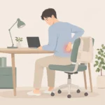 책상에 앉아 허리 아래쪽을 손으로 짚고 있는 사람과 의자 등받이에 걸쳐진 허리 복대