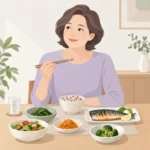 식탁에 놓인 통곡물밥과 구운 등푸른생선, 채소 반찬을 앞에 두고 앉아 있는 중년 여성