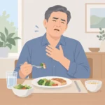 중년 남성이 식사 중 음식을 삼키기 힘들어하며 가슴 위쪽을 손으로 누르는 모습